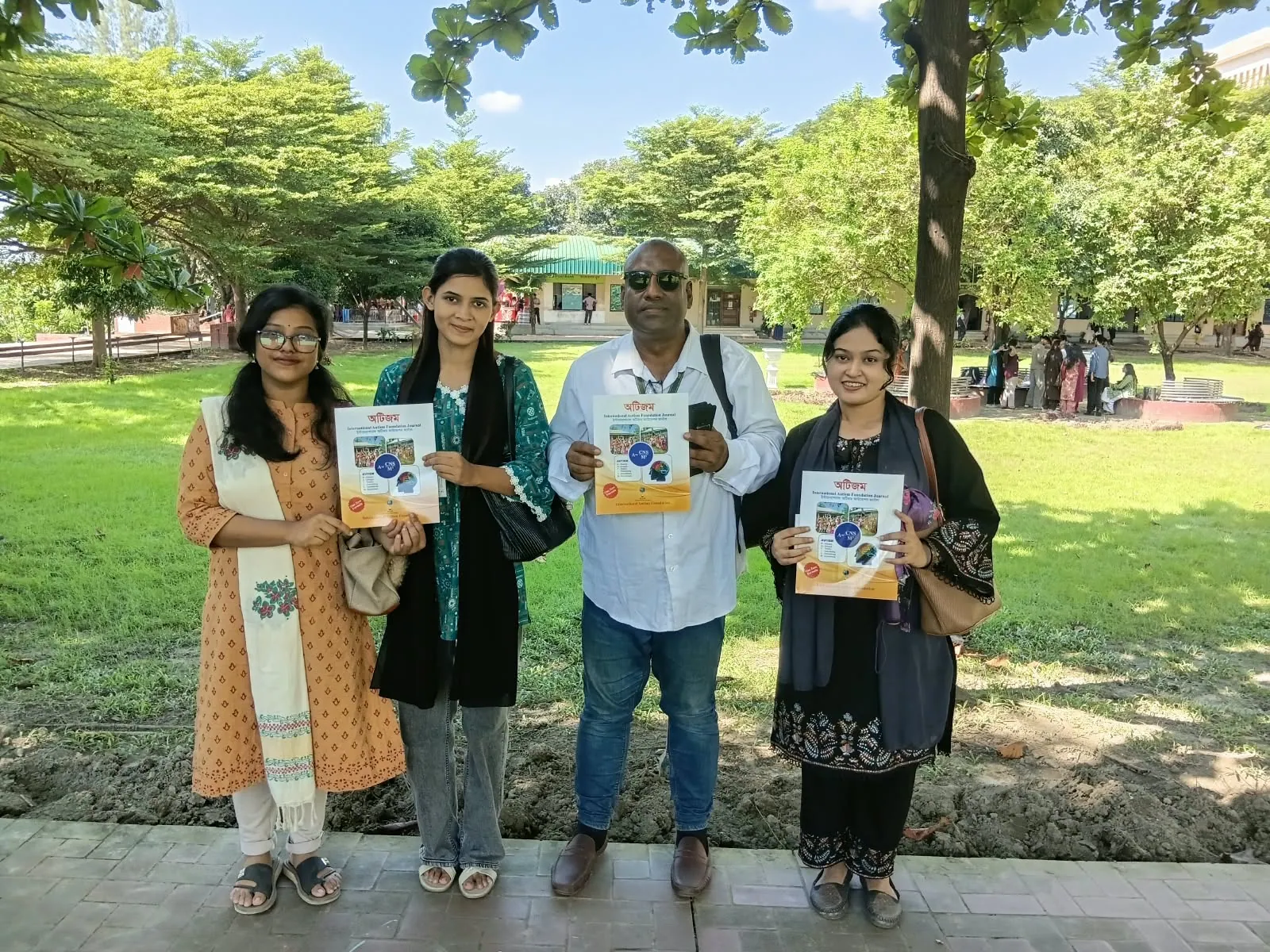 Four visitors holding copies of the Foundation's autism book on a green lawn