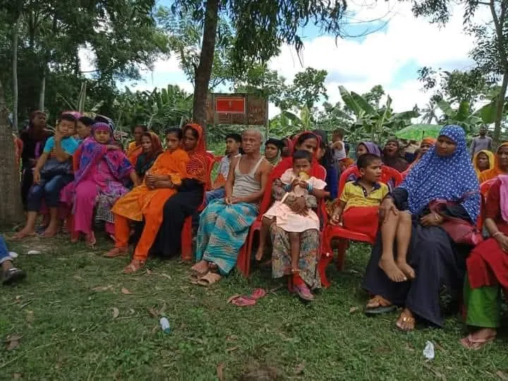 Mothers and children seated on plastic chairs on the grass at an outdoor gathering