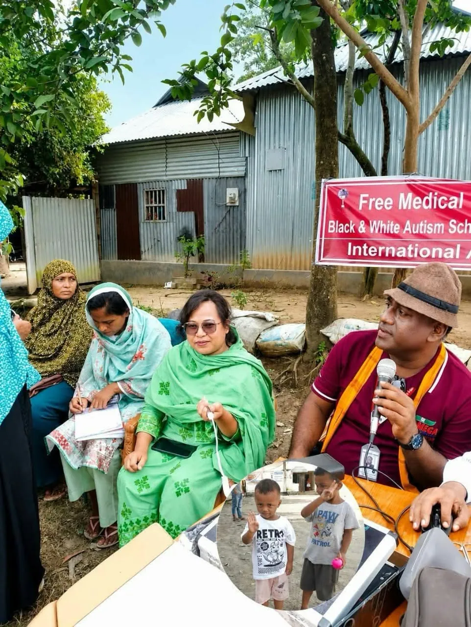 A free medical camp in progress, with mothers seated on the ground beside the camp banner
