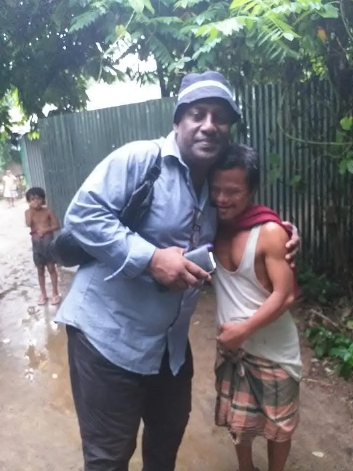 The Chairman embracing a man in the rain beside a tin fence