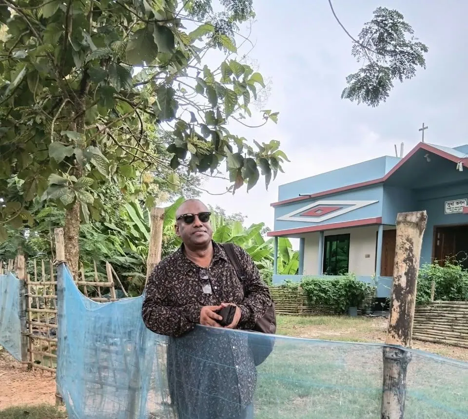 The Chairman beside a bamboo and net fence with a blue house behind