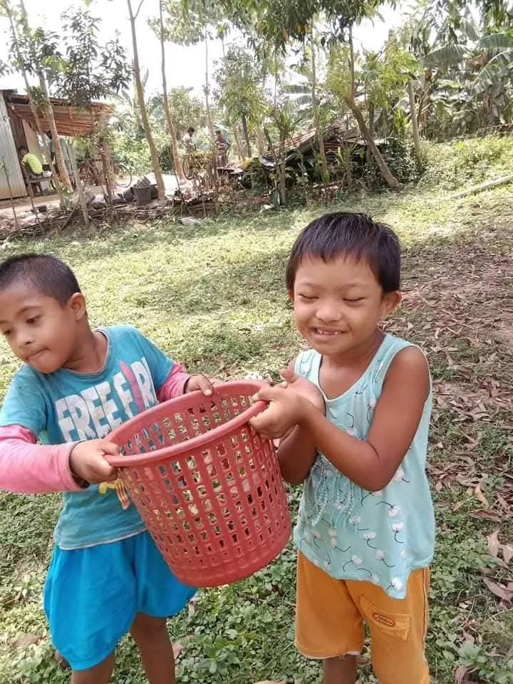 Two children laughing as they carry a red basket outdoors