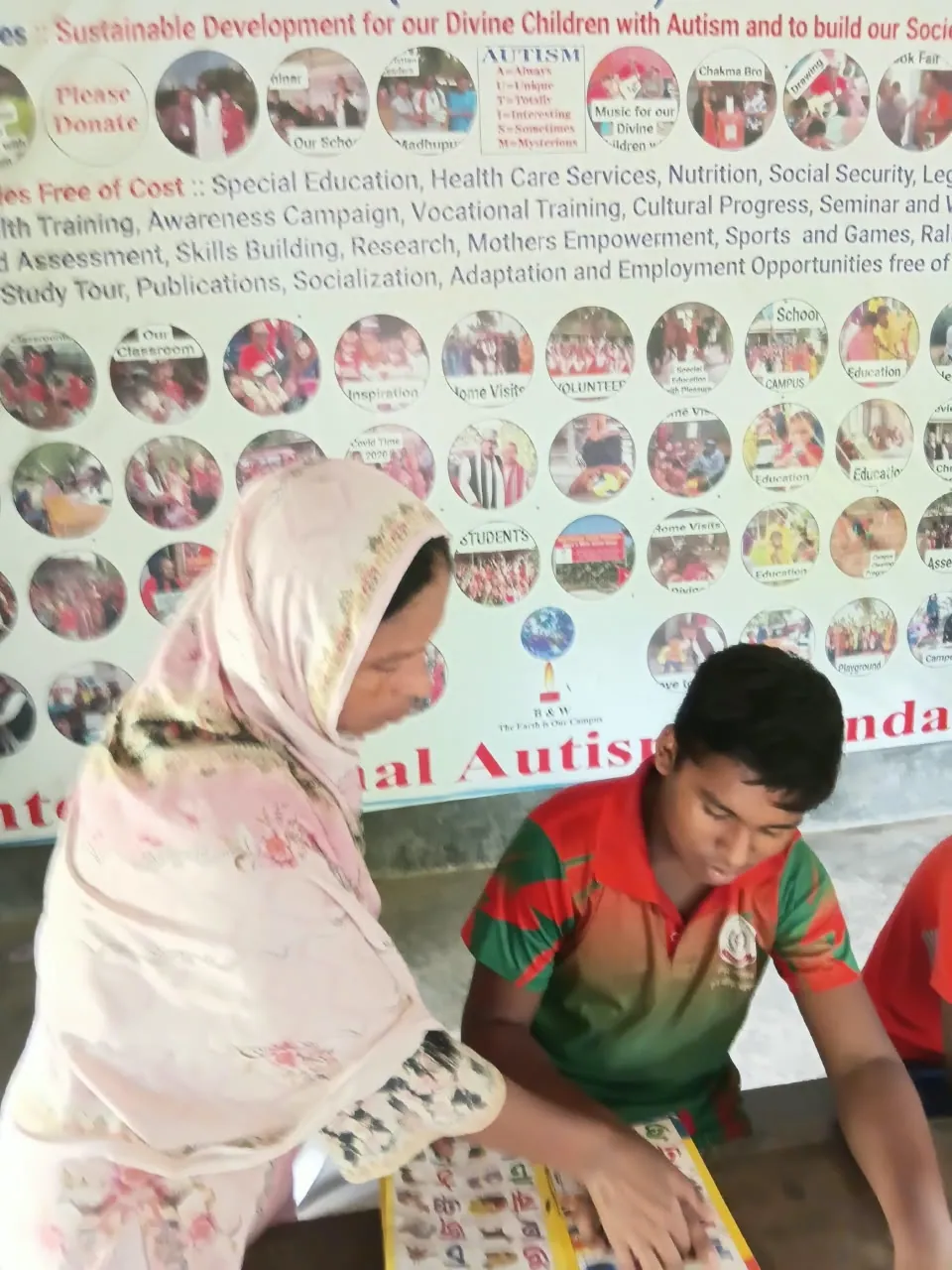 A boy in a red-and-green jersey studying picture cards with a helper