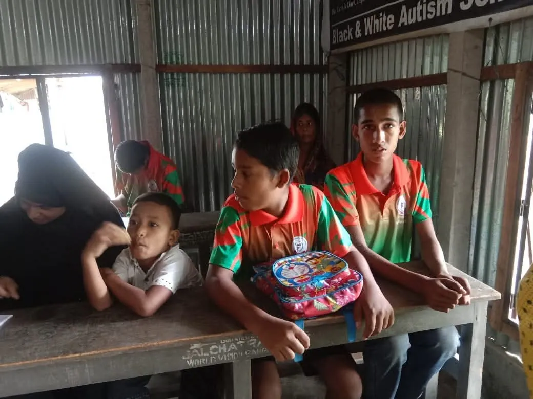 Students at classroom desks in a tin-walled schoolroom
