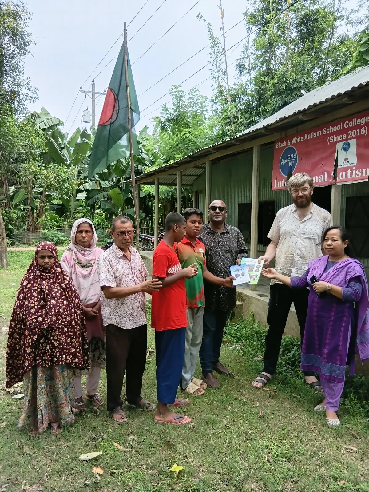 Villagers and visitors gathered on the grass outside the school under the national flag
