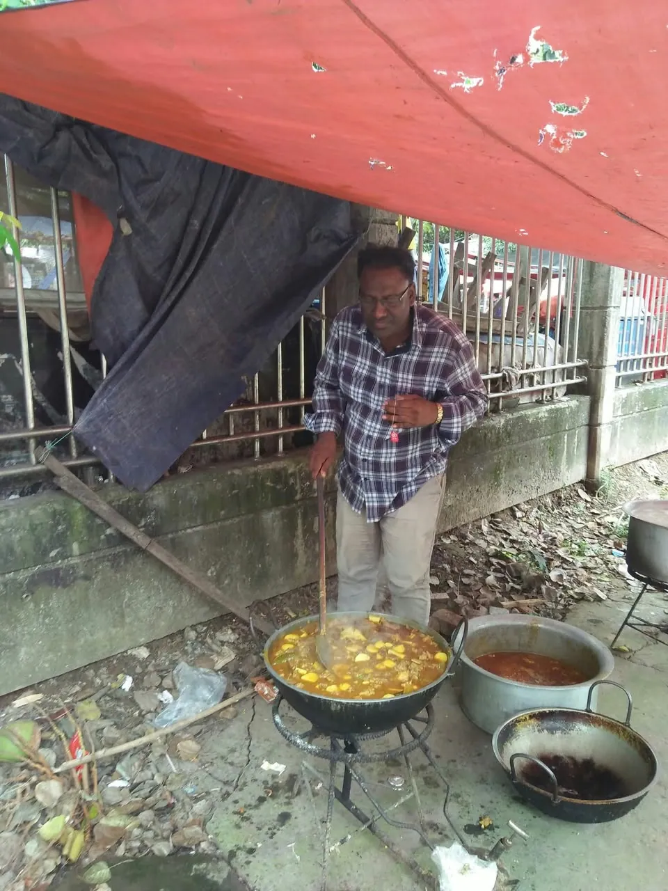 Stirring a large pan of curry over an open fire under a tarp