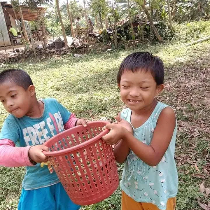Two children laughing as they carry a red basket
